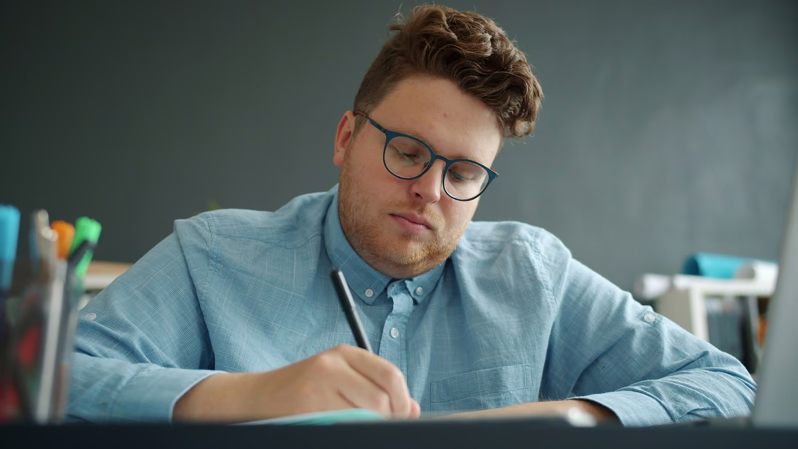 A student in glasses writing answers in a notebook