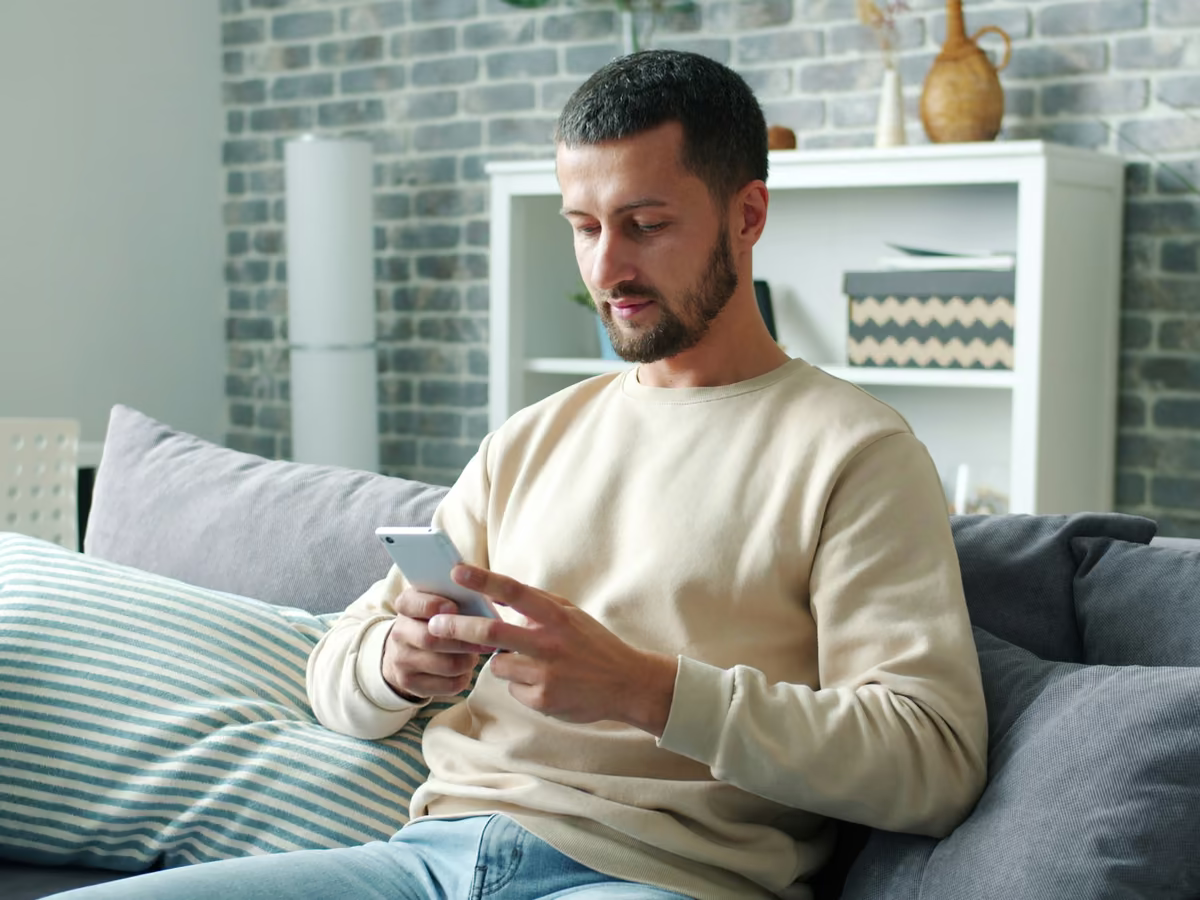 A father on the sofa at home, reading a message on his phone