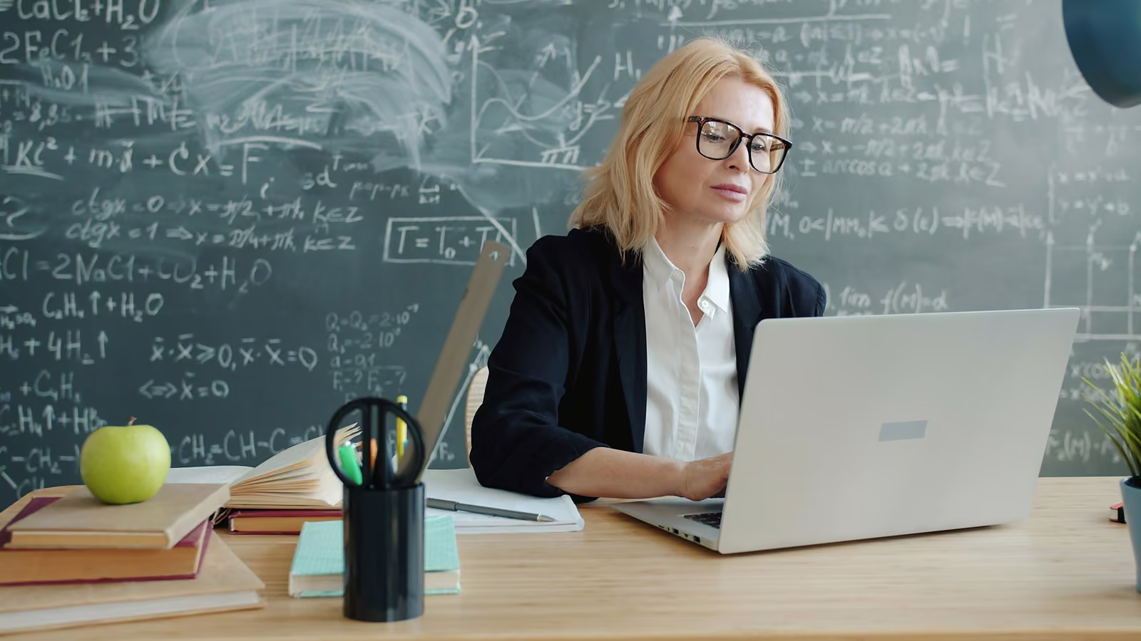 A teacher working on a laptop in front of a chalkboard