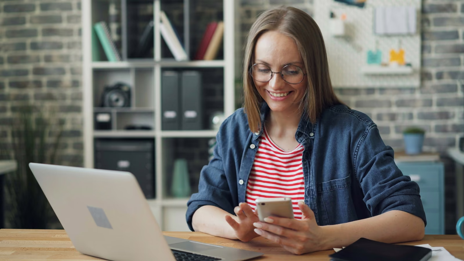 A teacher at her laptop, smiling as she reads a message on her phone
