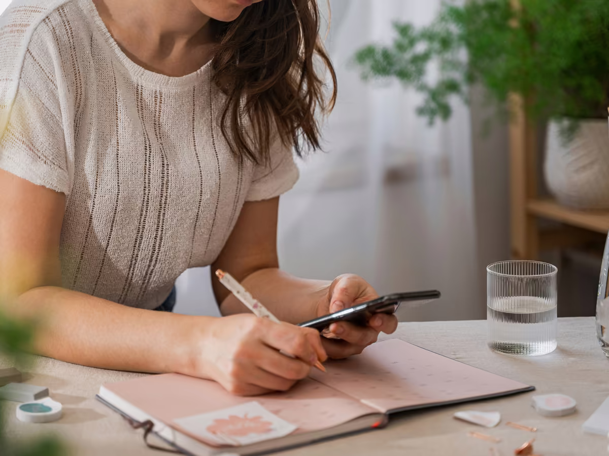 A teacher at her desk, phone in hand, writing the week into a planner