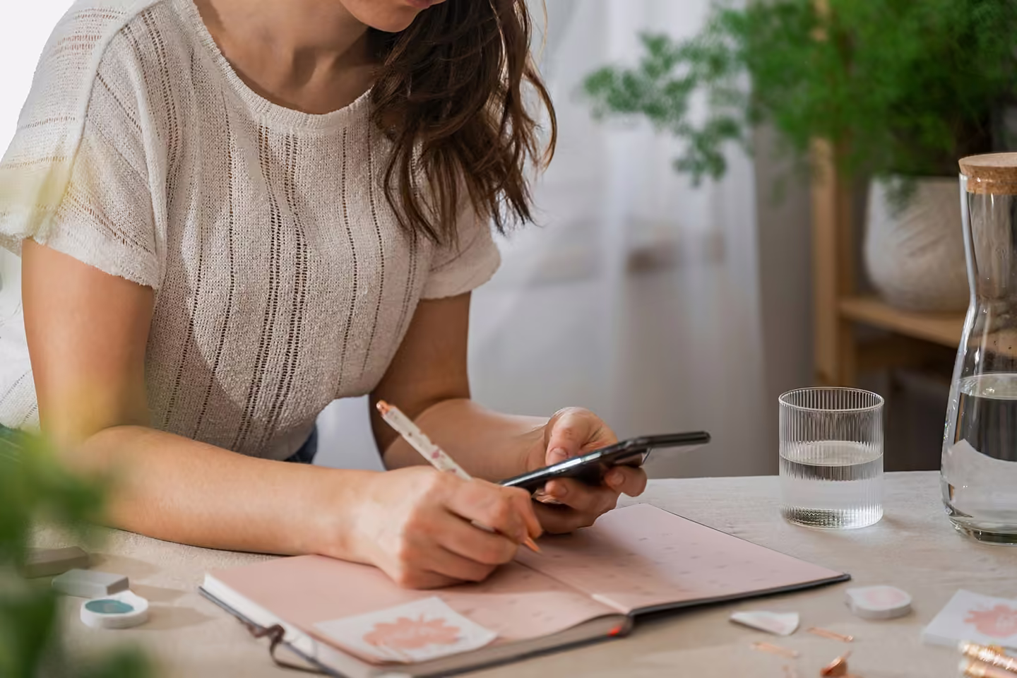 A teacher at her desk, phone in hand, writing the week into a planner